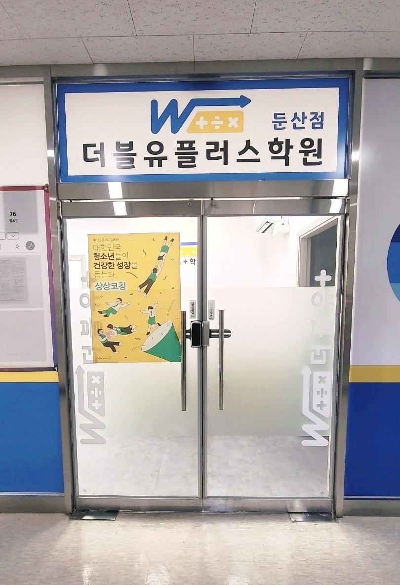 둔산점 더블유플러스학원 수학전문관 입구 — 파란 간판과 유리문, 청소년 성장 코칭 포스터가 붙은 출입구